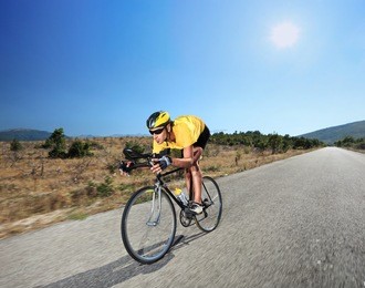 cyclist riding a bike on an open road in macedonia with a sun in the background