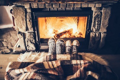feet in woollen socks by the christmas fireplace. couple sitting under the blanket, relaxes by warm fire and warming up their feet in woollen socks. winter and christmas holidays concept.