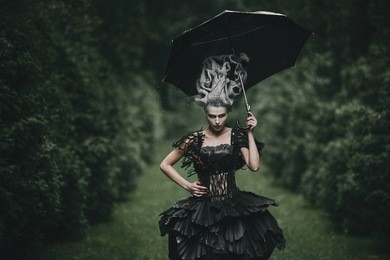 woman dressed like a hero from 'alice in wonderland' poses with black umbrella in a green park