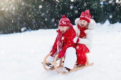 little girl and boy enjoy a sleigh ride. child sledding. toddler kid riding a sledge. children play outdoors in snow. kids sled in alps mountains in winter. outdoor fun for family christmas vacation.