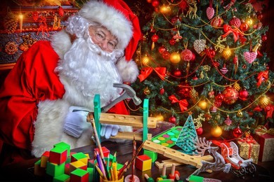 workshop of santa claus. portrait of santa claus making christmas gifts at home near beautiful christmas tree and a fireplace.