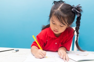 asian little girl children happy doing her homework sitting writing in desk at home. family , education concept