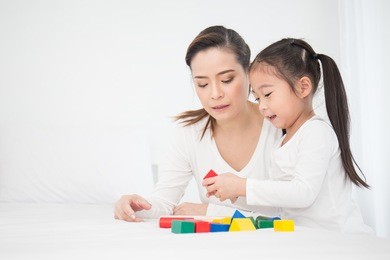 portrait of asian little cute girl playing colorful blocks with her mother over white background. learning by playing education home school concept. mother teaching her daughter to play blocks.