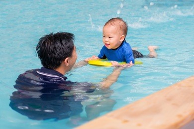 asian father take cute little asian 18 months / 1 year old toddler baby boy child to swimming class in thailand, happy infant enjoying his first swim in pool with his dad, selective focus