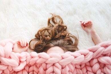 young woman with long brown hair sleeping under warm knitted peach color throw blanket