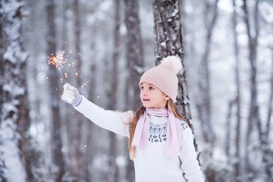 kid girl 5-6 year old holding firework outdoors over winter background. happiness. holiday season. christmas time. 