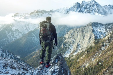 man hiker with a backpack on top of the mountain back, looking at the snow slope. the concept of active relaxation, motivation and goal achievement
