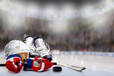 low angle view of hockey helmet, skates; gloves; stick and puck on ice with deliberate shallow depth of field on brightly lit stadium background and copy space.