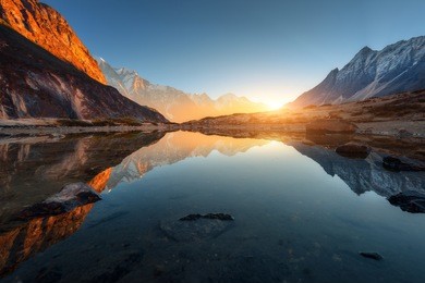 beautiful landscape with high rocks with illuminated peaks, stones in mountain lake, reflection, blue sky and yellow sunlight in sunrise. nepal. amazing scene with himalayan mountains. himalayas
