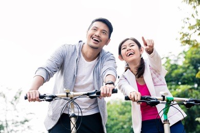 young asian couple laughing together while riding bicycles outdoors in summer 