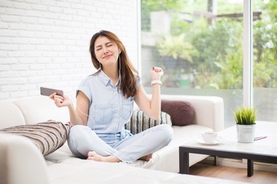 happy young woman with earphone dancing and listening to music on sofa