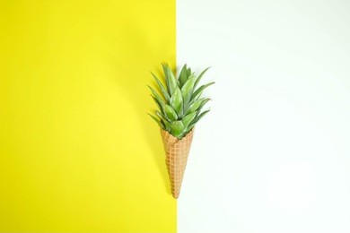 ice cream cone with pineapple leaves on yellow and white background, fruit and candy concept. flat lay.