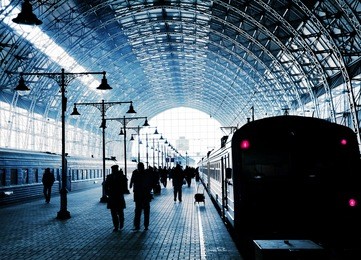 covered railway station with trains and silhouettes of hurrying people