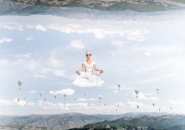 young woman keeping eyes closed and looking concentrated while meditating on cloud among flying aerostats and between two nature worlds.