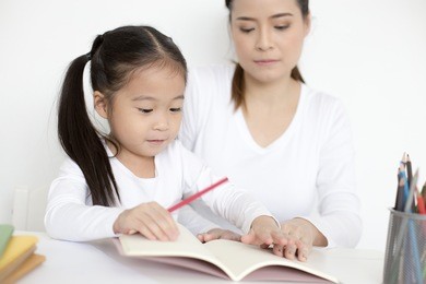attractive little girl writing book. mom teaching her at home. children lifestyle, education concept.