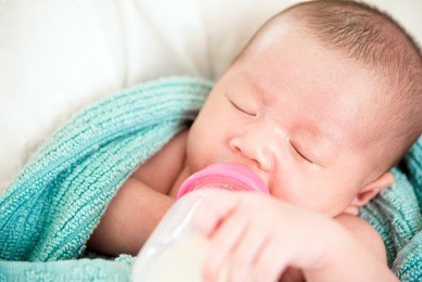 innocent beautiful sleeping newborn little baby drinking milk from feeding bottle in mother arms