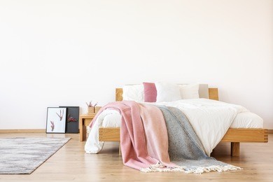 pink and grey blankets on bed, carpet and posters in simple bedroom with copy space on white wall