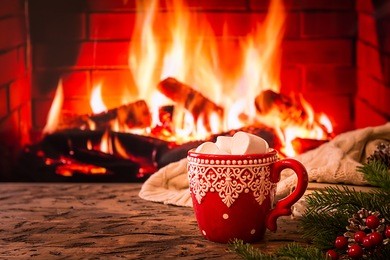 mug of hot chocolate or coffee with marshmallows in a red mug on vintage wood table in front of fireplace as a background. christmas or winter warming drink.