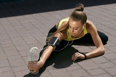 fitness. woman doing workout exercise on street. beautiful fit girl wearing fitness tracker, headphones and armband phone case stretching her long legs outdoors. sports devices. high resolution