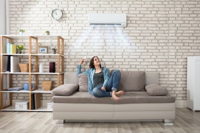 happy young woman holding remote control relaxing under the air conditioner