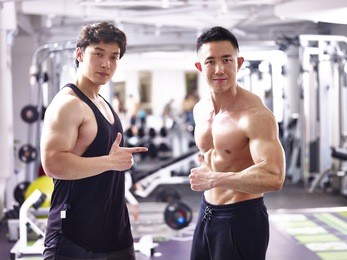 two asian bodybuilders posing in gym showing muscles.