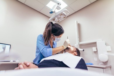female dentist examining a patient with tools in dental clinic. doctor doing dental treatment on man's teeth in the dentists chair.