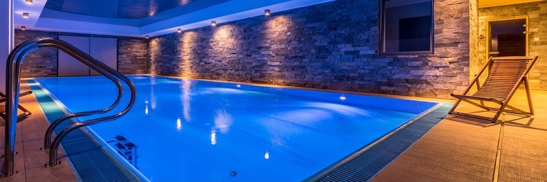 panoramic view of luxurious swimming pool with brick wall and deck chair