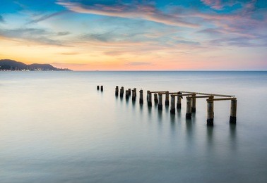 long exposure sunset seascape with old jetty formation in foreground, robina beach, pulau pinang, malaysia. soft focus, motion blur due to long exposure shot.