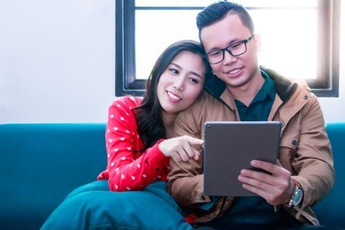 portrait in love couple:beautiful girl is pointing at the tablet screen. lover is looking something on internet. a beautiful girl nestles on her boyfriend shoulder and sitting on the couch at a room