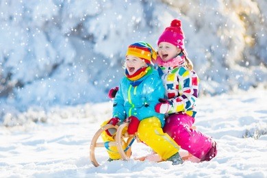 little girl and boy enjoying sleigh ride. child sledding. toddler kid riding a sledge. children play outdoors in snow. kids sled in snowy park in winter. outdoor fun for family christmas vacation.