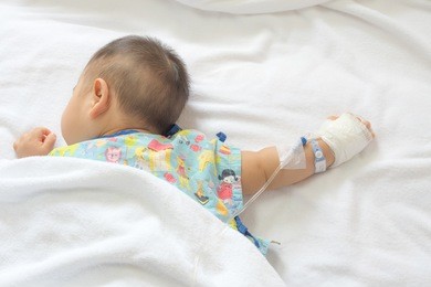 hands of a little boy attaching intravenous tube to patient's hand in hospital bed.