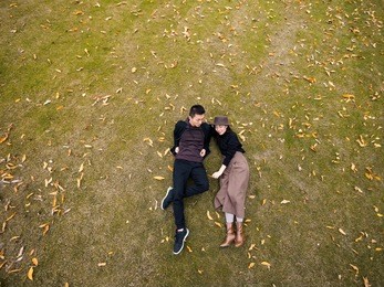 bird's view of couple of chinese young people laying on the grass field covered with yellow leaves in autumn day, high angle view.
