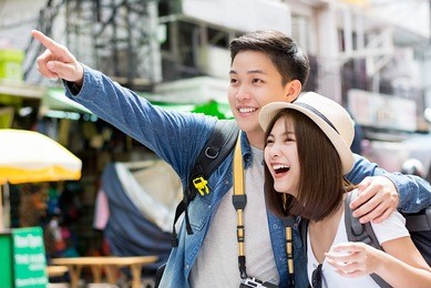 young happy asian couple tourist backpackers enjoy visiting khao san road on summer holiday traveling in bangkok, thailand