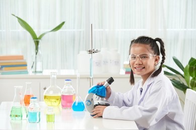 smiling schoolgirl using microscope at chemistry class