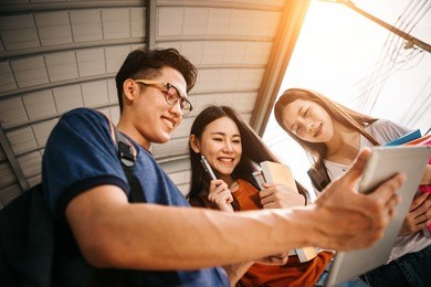 a group of young or teen asian student in university smiling and reading the book and look at the tablet or labtop computer in summer holiday.