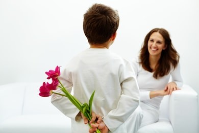 rear view of lad with bunch of beautiful tulips behind back preparing nice surprise for his mother