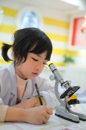 little asian kid writing report after looking into microscope