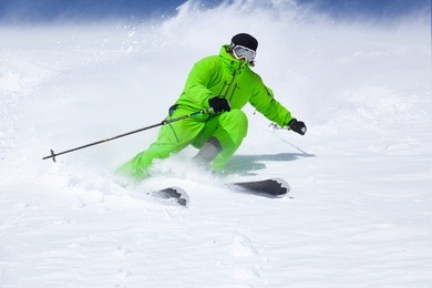 a man is skiing on the slope, wearing brigh green suit. good skiing day, blue sky on the background.