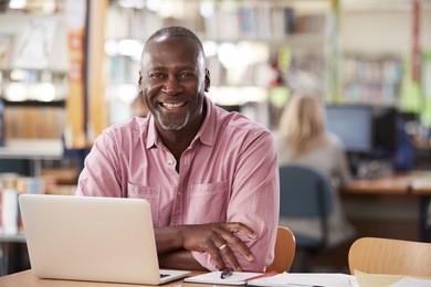portrait of mature male student using laptop in library