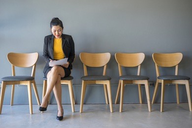 a woman sitting in a chair reading a document while waiting for a job interview in the waiting room.