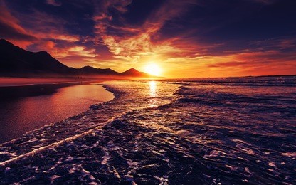 beach sunset with endless horizon and lonely figures in the distance, and incredible foamy waves. volcanic hills in the background
