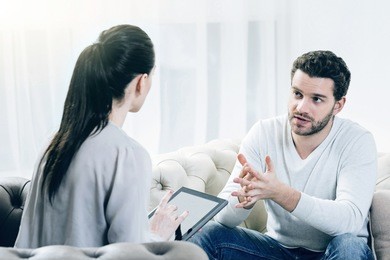 professional specialist. serious smart attentive psychologist sitting opposite her patient and listening to his problems while holding a tablet