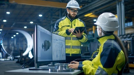 inside the heavy industry factory female industrial engineer works on personal computer she designs 3d turbine model, her male colleague talks with her and uses tablet computer.