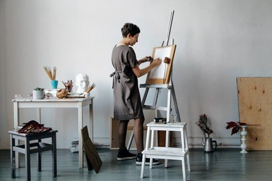female artist in her spacious white studio working with watercolor painting.  natural lighting. disclosure of creativity concept. horizontal composition.