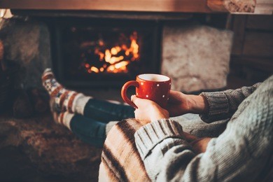feet in woollen socks by the christmas fireplace. woman relaxes by warm fire with a cup of hot drink and warming up her feet in woollen socks. cozy atmosphere. winter and christmas holidays concept.