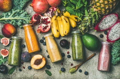 flat-lay of colorful smoothies in bottles with fresh tropical fruit and superfoods on concrete background, top view. healthy, clean eating, vegan, vegetarian, detox, dieting breakfast food concept