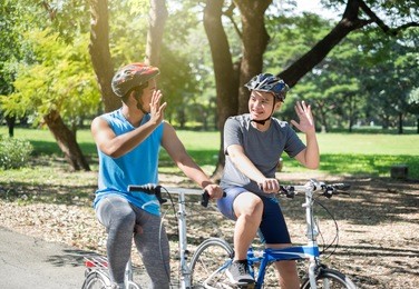 asian boy with friend ride a bike/bicyle at outdoor green park in summer say hi/bye each other