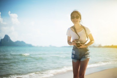portrait of asian young teenager woman. chill out at the beach with blue sea and blue sky. wearing a sunglasses. filtered image. selective focus. light effect added. happy summer travel concept
