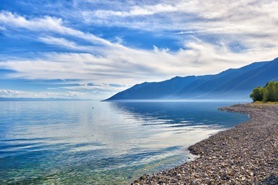 pebble shore of lake baikal and taiga mountains in distance. irkutsk region. russia