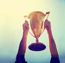 a man holding up a gold trophy cup as a winner in a competition toned with a retro vintage instagram filter effect app or action (shallow dof on writing)